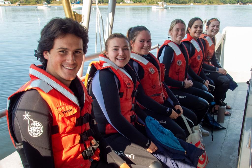一群身穿橙色救生衣的学生在一艘欧盟船上排成一排