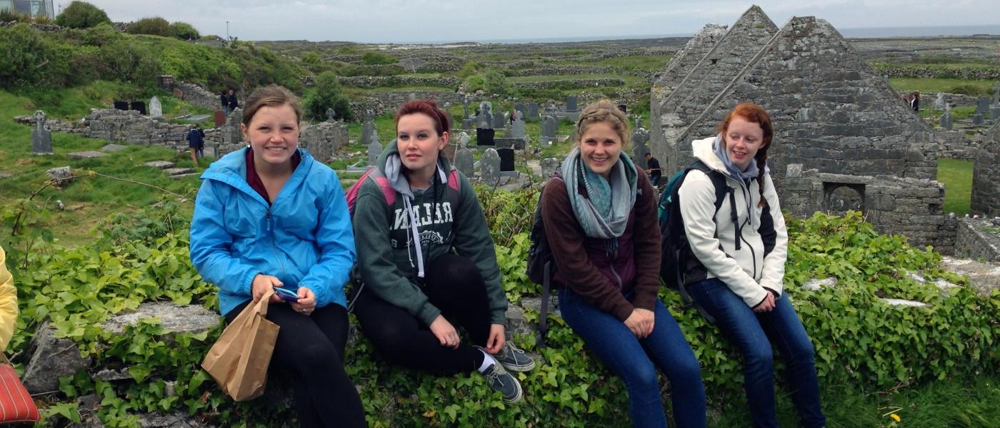 爱尔兰，一群大学学生坐在起伏的山坡墓地的石墙上
